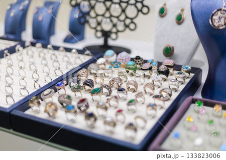 Numerous rings and earrings are arranged on display in a jewelry store. Each piece features unique designs, colorful gemstones, and delicate details, attracting attention from shoppers Numerous rings and earrings are arranged on display in a jewelry store. Each piece features unique designs, colorful gemstones, and delicate details, attracting attention from shoppers 133823006