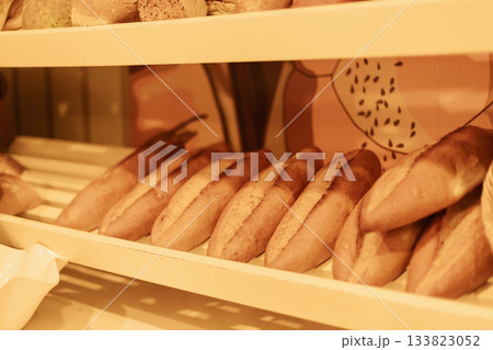 Soft, golden loaves of bread are neatly arranged on a wooden shelf in a charming bakery. The warm atmosphere invites customers to enjoy fresh baked goods Soft, golden loaves of bread are neatly arranged on a wooden shelf in a charming bakery. The warm atmosphere invites customers to enjoy fresh baked goods 133823052
