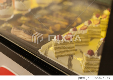 Delicious layered cakes and pastries are beautifully arranged in a bakery display case. Each treat features unique decorations, attracting customers with their sweet appeal Delicious layered cakes and pastries are beautifully arranged in a bakery display case. Each treat features unique decorations, attracting customers with their sweet appeal 133823075