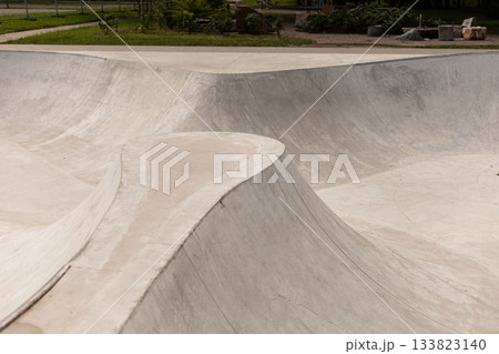 A modern skatepark showcases flowing concrete surfaces and ramps designed for skateboarders and BMX riders to practice tricks and skills. The location features greenery nearby 133823140