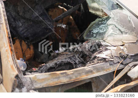 The remains of a burnt car reveal extensive fire damage inside the vehicle's cabin. Charred materials and broken glass create a stark scene in an abandoned location The remains of a burnt car reveal extensive fire damage inside the vehicle's cabin. Charred materials and broken glass create a stark scene in an abandoned location 133823160