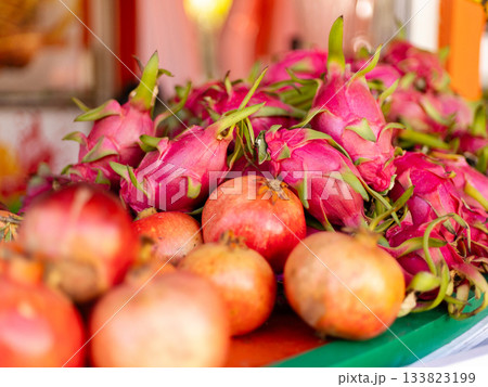 Fresh dragon fruits and pomegranates are neatly arranged at a bustling market stall. The bright colors of the fruits stand out in the warm morning light, attracting customers Fresh dragon fruits and pomegranates are neatly arranged at a bustling market stall. The bright colors of the fruits stand out in the warm morning light, attracting customers 133823199