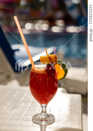 A vibrant tropical cocktail sits on a table by the poolside, featuring colorful garnishes like pineapple, orange, and cherries, perfect for a sunny day of relaxation A vibrant tropical cocktail sits on a table by the poolside, featuring colorful garnishes like pineapple, orange, and cherries, perfect for a sunny day of relaxation 133823222