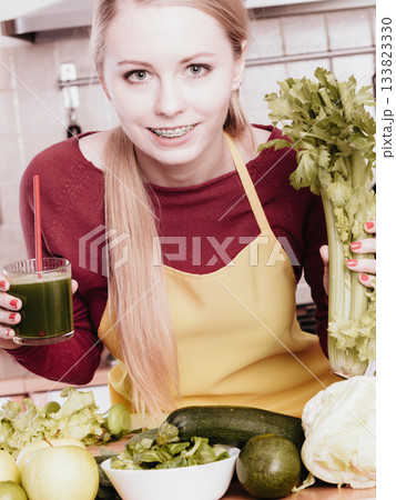 Woman in kitchen holding vegetable smoothie juice 133823330