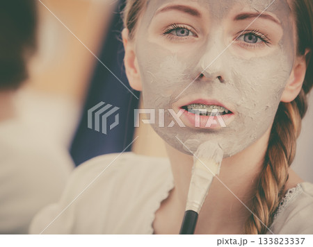 Woman applying with brush clay mud mask to her face 133823337