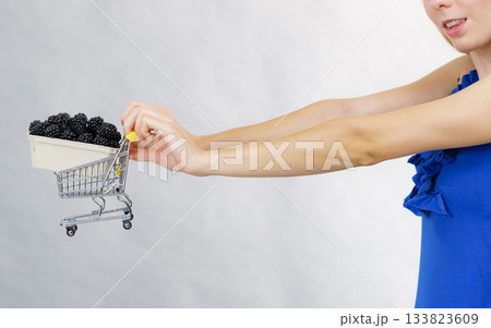 Hand holds blackberry fruits in shopping cart 133823609