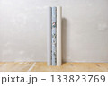 Three rolls of wallpaper stand against a gray wall ready for wallpapering. 133823769