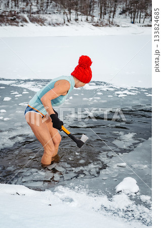 Senior woman breaking ice for winter swimming on frozen lake. Senior woman breaking ice for winter swimming on frozen lake. 133824685