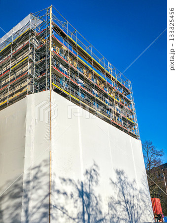 Building under renovation covered with scaffolding and protective sheeting against blue sky 133825456