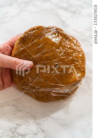 Close-up of a single portion of Zesty Orange Gingerbread Cookie Dough wrapped in plastic wrap, ready to be chilled. The smooth dough surface hints at a rich, flavorful result after baking. Close-up of a single portion of Zesty Orange Gingerbread Cookie Dough wrapped in plastic wrap, ready to be chilled. The smooth dough surface hints at a rich, flavorful result after baking. 133825618