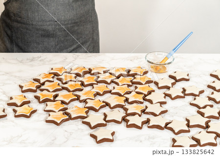A wide spread of golden-decorated gingerbread star cookies arranged on a white surface, highlighting their intricate royal icing and elegant gold luster dust finish. 133825642