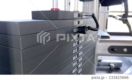 Side view of gym machine weight stack showing numbers and weight levels. The fitness equipment is part of a modern strength training setup. 133825666