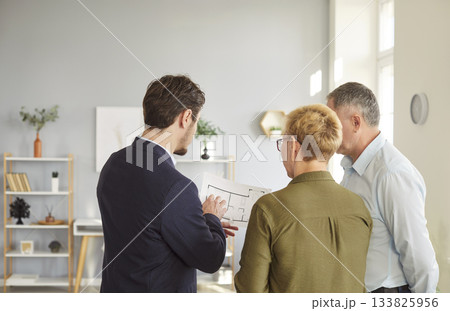 Man architect or designer showing to senior couple blueprint with design project Man architect or designer showing to senior couple blueprint with design project 133825956