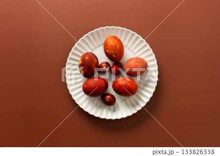 Vibrant Easter eggs in various shades of red and orange are beautifully arranged on a white plate, adding charm to the festive atmosphere of the season Vibrant Easter eggs in various shades of red and orange are beautifully arranged on a white plate, adding charm to the festive atmosphere of the season 133826338