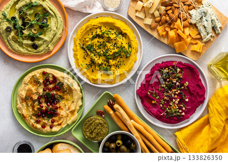 A variety of hummus flavors including turmeric, classic, and broccoli are served with fresh bread, nuts, and garnishes on a colorful charcuterie board, perfect for sharing A variety of hummus flavors including turmeric, classic, and broccoli are served with fresh bread, nuts, and garnishes on a colorful charcuterie board, perfect for sharing 133826350