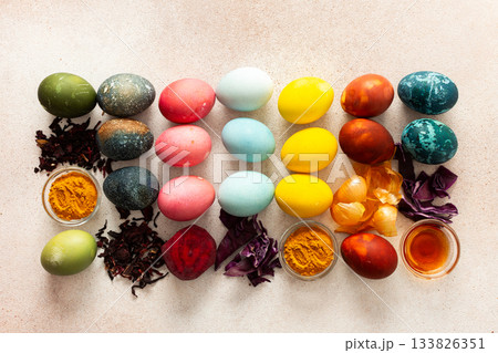 Brightly colored Easter eggs are lined up in a creative arrangement, surrounded by natural dyes made from plants, such as beets, turmeric and hibiscus, red cabbage and onion peel, vinegar Brightly colored Easter eggs are lined up in a creative arrangement, surrounded by natural dyes made from plants, such as beets, turmeric and hibiscus, red cabbage and onion peel, vinegar 133826351