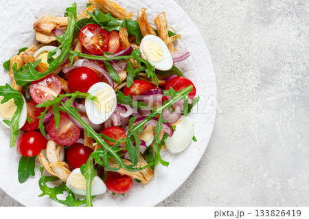 a warm salad with fried chicken fillet, arugula and cherry tomatoes, and boiled quail eggs, on a white plate, no people. a warm salad with fried chicken fillet, arugula and cherry tomatoes, and boiled quail eggs, on a white plate, no people. 133826419