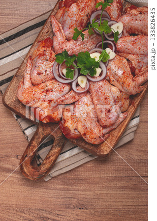 Chicken wings, marinated and laid out on a wooden platter, ready for cooking, grilling or baking, in a home kitchen, there are no people Chicken wings, marinated and laid out on a wooden platter, ready for cooking, grilling or baking, in a home kitchen, there are no people 133826435