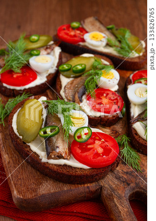 open sandwiches with sprats, vegetables and herbs, on a wooden board, breakfast, snack, 133826765