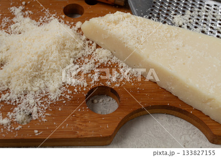Freshly sliced and grated cheese, parmesan cheese, on a wooden chopping board, rustic style, no people 133827155
