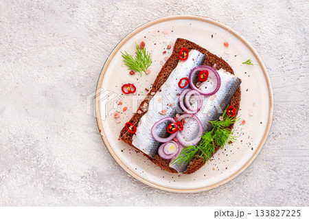 sandwiches , Herring fish, on dark rye bread, sprinkled with onion, chili pepper and herbs, on a light plate 133827225