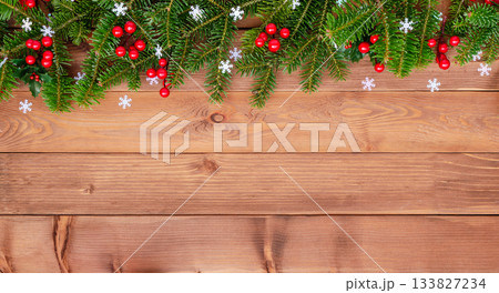 Natural Christmas border with fir branches and red holly berries on wooden background Natural Christmas border with fir branches and red holly berries on wooden background 133827234