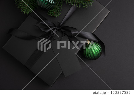 Black Christmas Gift Box with Satin Ribbon and Green Ornaments on Dark Holiday Background Black Christmas Gift Box with Satin Ribbon and Green Ornaments on Dark Holiday Background 133827583
