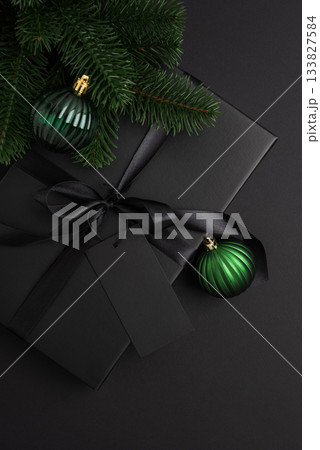 Black Christmas Gift Box with Satin Ribbon and Green Ornaments on Dark Holiday Background 133827584