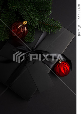 Black Christmas Gift Box with Satin Ribbon and Red Ornaments on Dark Holiday Background 133827586