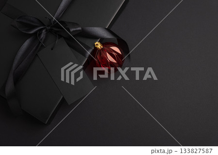 Black Christmas Gift Box with Satin Ribbon and Red Ornaments on Dark Holiday Background 133827587