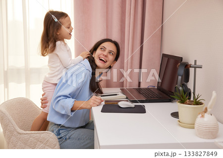 Happy mother working from home laughing while child plays and distracts her 133827849