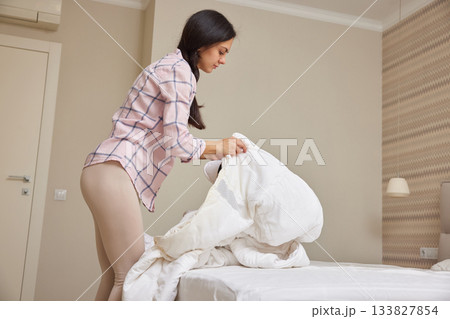 Woman making her bed, tidying up bedroom for a fresh start to the day Woman making her bed, tidying up bedroom for a fresh start to the day 133827854