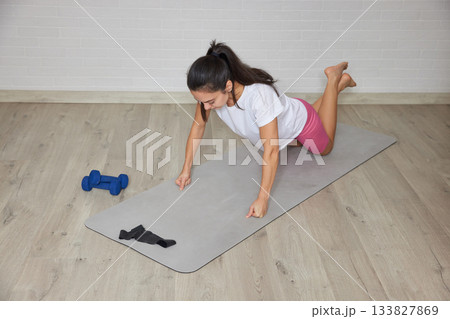 Woman exercising on yoga mat with dumbbells nearby, practicing push-ups for fitness Woman exercising on yoga mat with dumbbells nearby, practicing push-ups for fitness 133827869