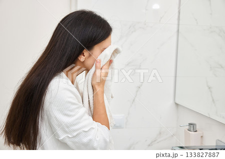 Young woman drying her face with a soft towel in a clean bathroom Young woman drying her face with a soft towel in a clean bathroom 133827887