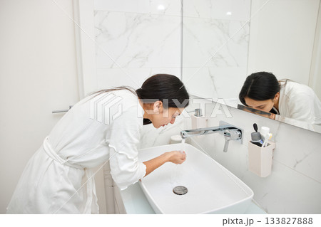 Woman in bathrobe rinsing face with water from a modern sink Woman in bathrobe rinsing face with water from a modern sink 133827888