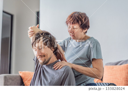 Older woman giving her adult son a shoulder and arm stretch massage at home, creating a warm family moment focused on care, relaxation and wellbeing. Wellness, support, bonding and healthy lifestyle 133828024