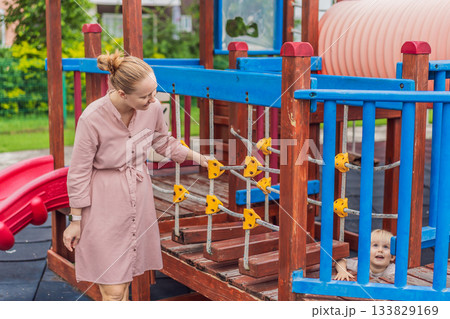 A mother playing with her young son at an outdoor playground, enjoying joyful family time and positive parenting moments. Childhood fun, bonding, laughter and carefree early years concept 133829169