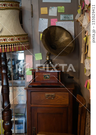 In a cozy corner, an elegant vintage gramophone rests atop a wooden cabinet. Colorful notes decorate the wall, hinting at cherished memories. In a cozy corner, an elegant vintage gramophone rests atop a wooden cabinet. Colorful notes decorate the wall, hinting at cherished memories. 133829411