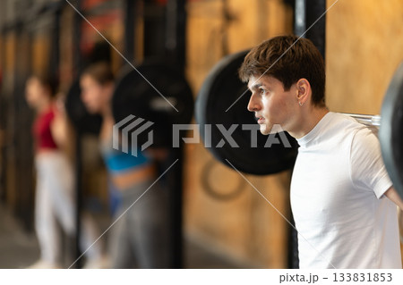 Slender guy trains muscles of arms and back using barbell and differentiated weighting in gym Slender guy trains muscles of arms and back using barbell and differentiated weighting in gym 133831853