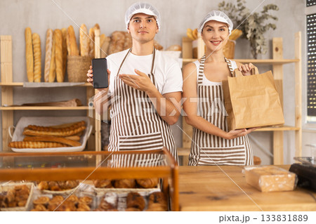 Salesman displays phone app standing next to saleswoman with paper bag Salesman displays phone app standing next to saleswoman with paper bag 133831889