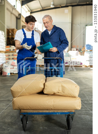 Guy check papers invoices with elderly male employee and revise availability of goods in stock 133831940