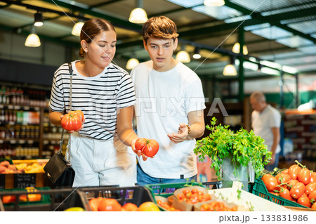 Cheerful young couple choosing ripe red tomatoes in store Cheerful young couple choosing ripe red tomatoes in store 133831986