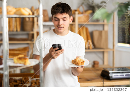 Interested guy using smartphone to analyze pastry in bakery 133832267
