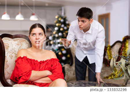 Emotional distressed young male and female screaming at each other while sitting on couch in front of Christmas tree in apartment Emotional distressed young male and female screaming at each other while sitting on couch in front of Christmas tree in apartment 133832296