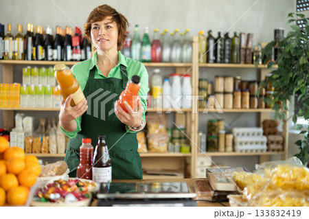 Woman seller stands in trading hall of store with goods in hand Woman seller stands in trading hall of store with goods in hand 133832419