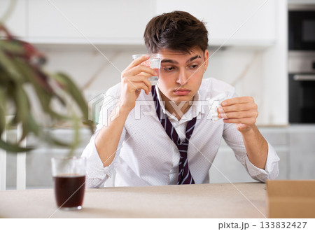 Young man after a severe hangover drinks pills for headache 133832427