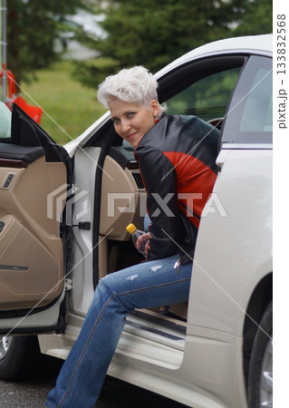 One girl, a blonde, is sitting in an expensive car and looking into the distance. It's autumn and raining outside. One girl, a blonde, is sitting in an expensive car and looking into the distance. It's autumn and raining outside. 133832568