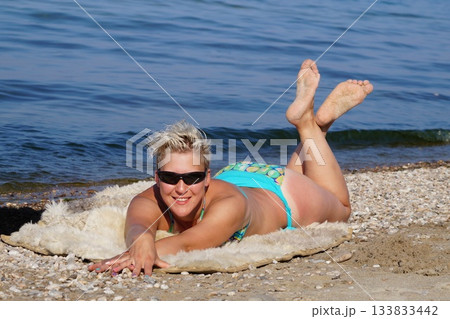 A blonde girl in glasses is looking at the sun, sunbathing, and laughing. She is lying on the shore of Lake Baikal. A blonde girl in glasses is looking at the sun, sunbathing, and laughing. She is lying on the shore of Lake Baikal. 133833442