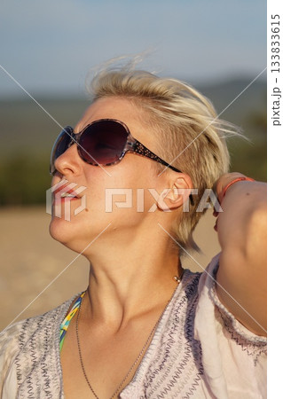 One girl, a blonde, in glasses and a swimsuit, looks at the sun, sunbathes, laughs. One girl, a blonde, in glasses and a swimsuit, looks at the sun, sunbathes, laughs. 133833615