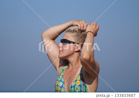One girl, a blonde, in glasses and a swimsuit, looks at the sun, sunbathes. She is happy. One girl, a blonde, in glasses and a swimsuit, looks at the sun, sunbathes. She is happy. 133833687